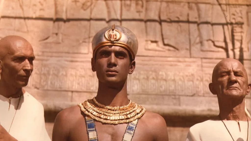 Фараон» (Faraon) 1966 г. Молодой мужчина с золотыми украшениями стоит посреди двух жрецов в белых одеждах.