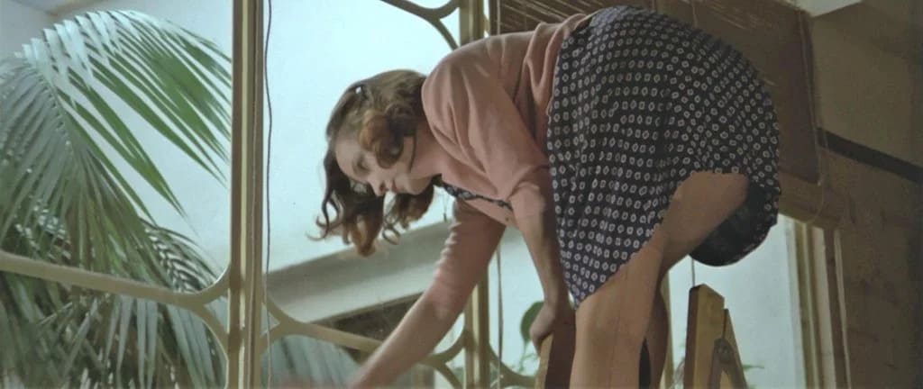 Коварство (Malizia) 1973 г. Молодая женщина нагибается, стоя у большого окна.